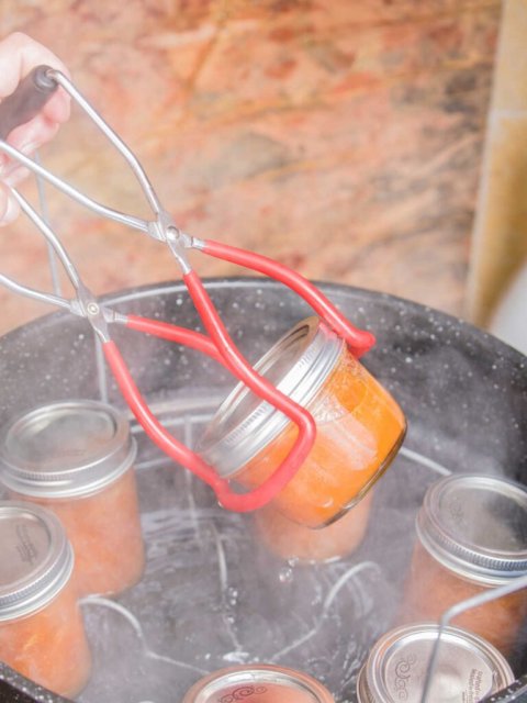 a jar lifter being used to remove a mason jar from a water bath canner.