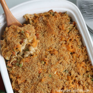 Old fashioned tune noodle casserole in white casserole dish and a wooden spoon lifting a piece out.