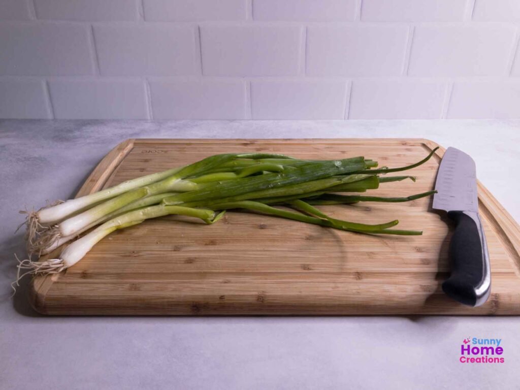 freshly washed green onions on a cutting board with a knife.