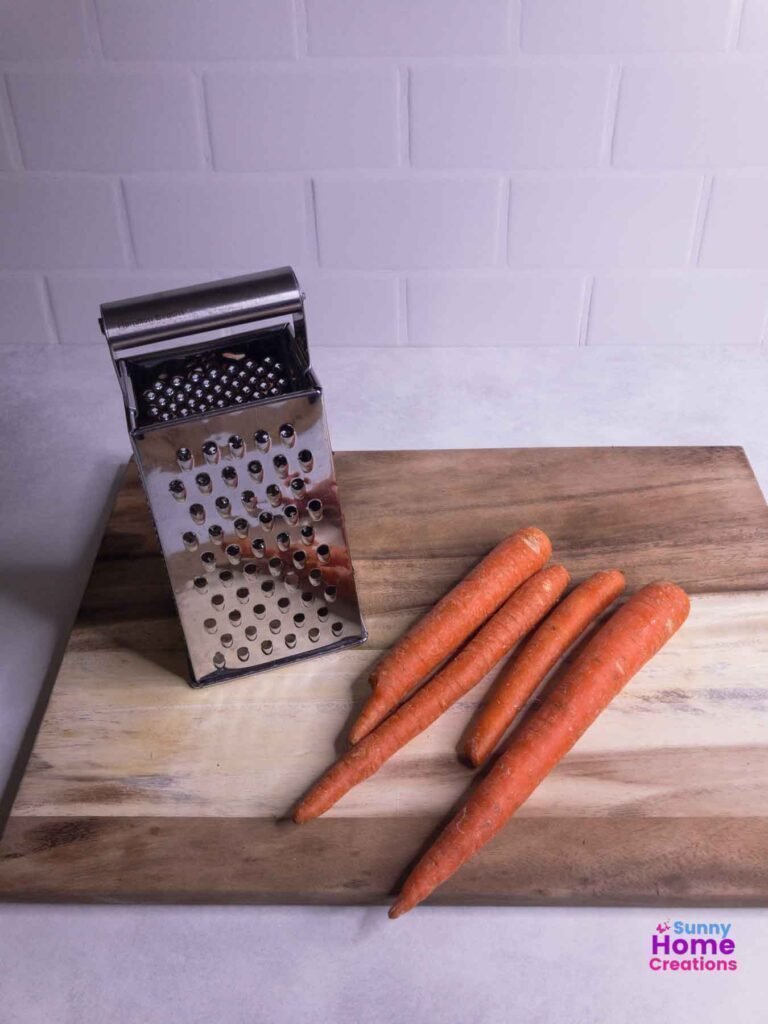 grater and carrots on top of cutting board.