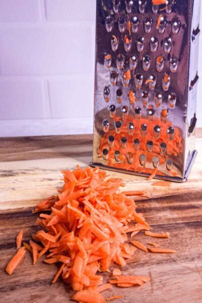 shredded carrots on a cutting board with a cheese grater in the background.